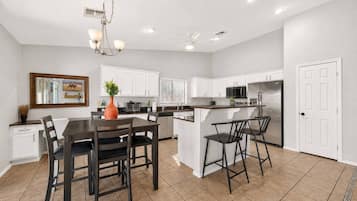 Una cocina moderna con muebles blancos, un comedor con mesa y sillas de madera oscura, y una isla central con taburetes de bar.
