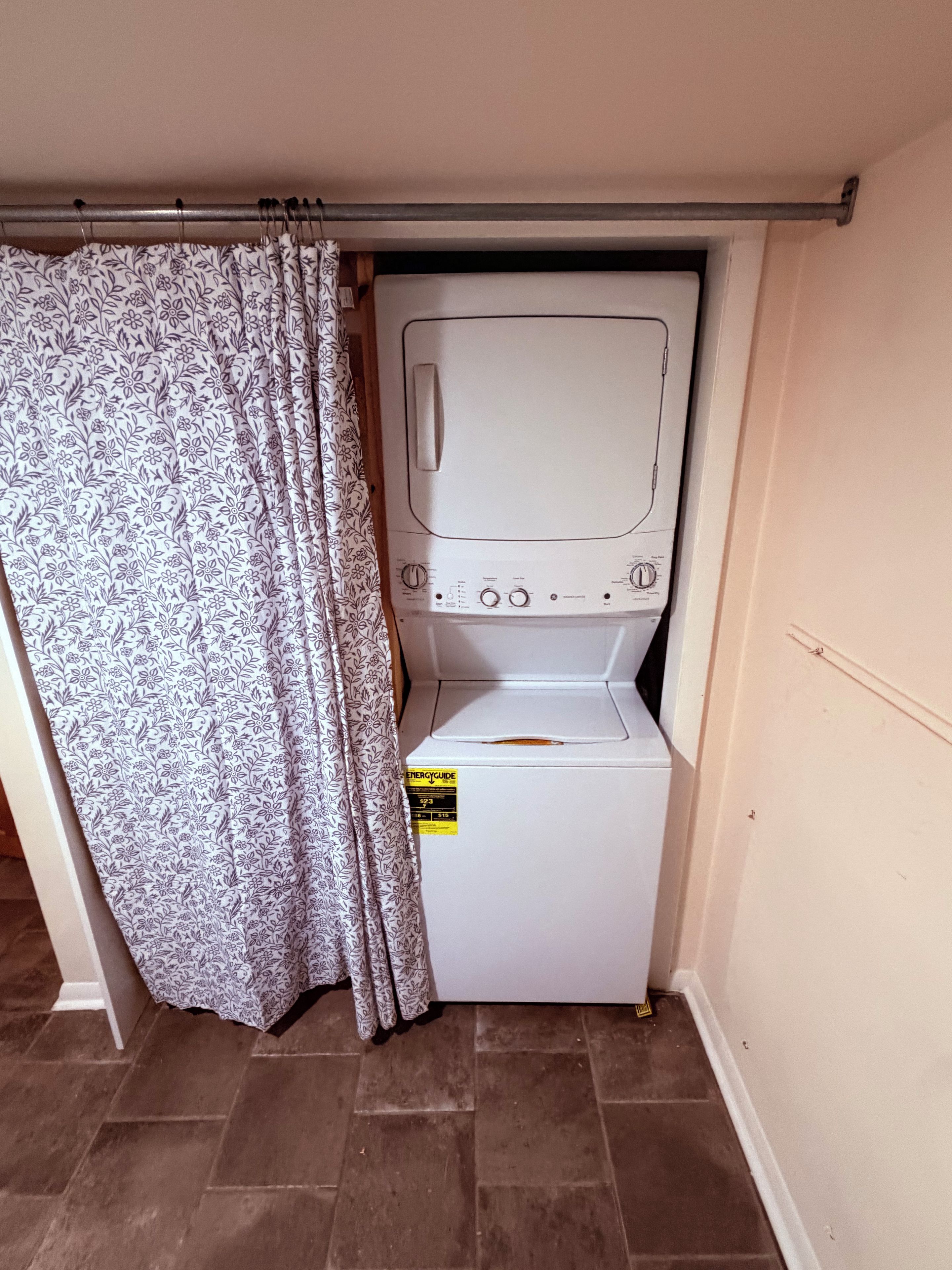 A compact laundry room with a washing machine and dryer, a curtain, and a tiled floor.