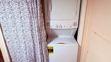 A compact laundry room with a washing machine and dryer, a curtain, and a tiled floor.