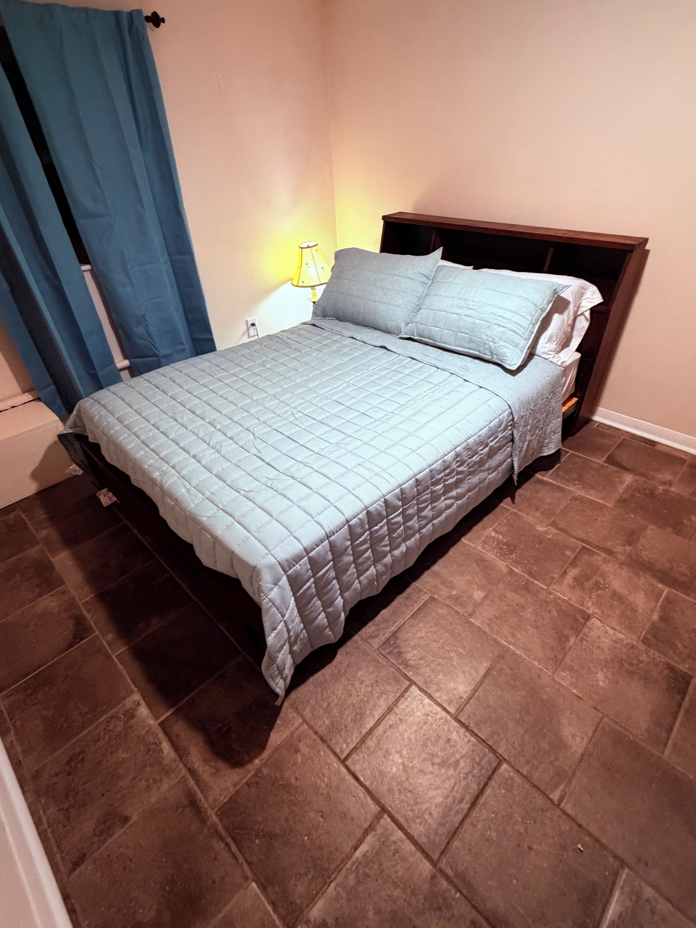 A bed with a quilted bedspread, a wooden headboard, and a lamp on a bedside table.