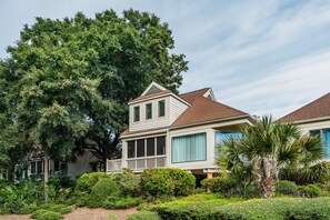 A two-story house with a covered porch, surrounded by lush greenery and a large tree. - 3-Minute walk to beach, Screen porch, Seabrook Island Retreat - 751 Spinnaker (Seabrook Island)