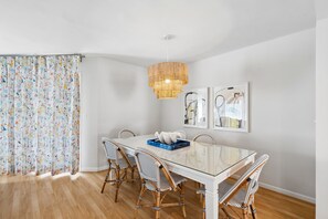 A dining area with a glass table, wicker chairs, a woven light fixture, and abstract wall art. - 3-Minute walk to beach, Screen porch, Seabrook Island Retreat - 751 Spinnaker (Seabrook Island)