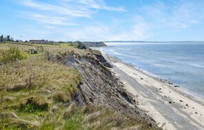 Ett kustlandskap med en sandstrand, gräsklädda klippor och fri utsikt över havet.
