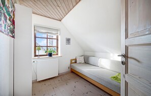 Et lille, hyggeligt rum med skråvægge, et vindue med udsigt, en radiator og en seng med pude.