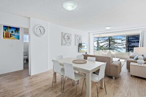 A modern living room with a dining area, white furniture, and artwork on the walls. - Goodwin Towers with Beach Views! (Gold Coast)
