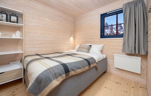 Une pièce de cabane en bois comprenant un lit, des étagères, une fenêtre et un radiateur.