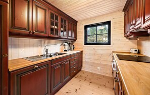 Eine Küche mit Holzausstattung, einer Edelstahlspüle und einem Fenster mit Blick ins Grüne.