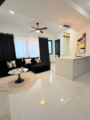 A modern living room with a sofa, a coffee table, and a dining area with a kitchen counter. - The Uptown Apartment 
Kingston’s Luxurious apartment perfect for up to 3 persons (Kingston)