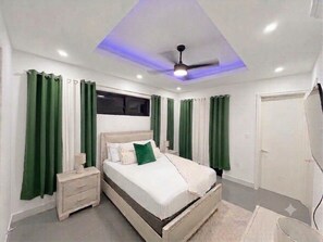 Ein Schlafzimmer mit Bett, Nachttisch, Vorhängen, Deckenventilator und Fenster.