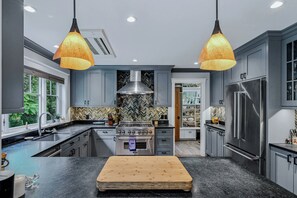 Une cuisine moderne avec des meubles gris, un réfrigérateur en acier inoxydable, une cuisinière à gaz et deux lampes suspendues.