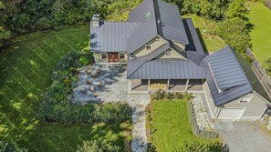 Une maison à deux étages dotée d’un patio en pierre, d’un foyer extérieur et d’un espace de détente extérieur abrité.