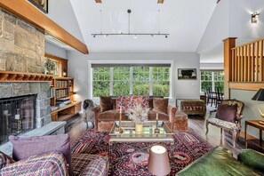 Un salon spacieux doté d’une cheminée, de grandes fenêtres et de différents types de sièges.