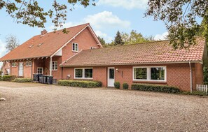 A two-story brick house with a red-tiled roof, a gravel driveway, and a white picket fence. - Nice home in ølgod with WiFi (Ølgod)
