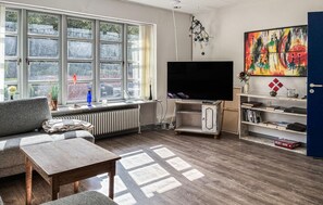 A living room with a large window, a flat-screen TV, a sofa, a coffee table, and a bookshelf. - Nice home in ølgod with WiFi (Ølgod)