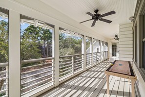 A covered porch with a ceiling fan, large windows, and a wooden table. - Next to Sand Hill Frog Pool, Carriage House, Arcade Games - Lake District (Santa Rosa Beach)