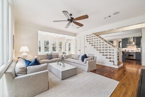 A spacious living room with a modern sofa set, a coffee table, and a ceiling fan. - Next to Sand Hill Frog Pool, Carriage House, Arcade Games - Lake District (Santa Rosa Beach)