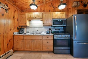 A kitchen with wooden cabinets, a stainless steel refrigerator, a microwave, an oven, and a coffee maker. - Year-Round Trail Access | Cozy Cabin on Lake (Cable)
