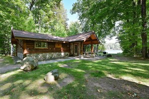 A rustic cabin with a stone foundation, a wooden deck, and a picnic table. - Year-Round Trail Access | Cozy Cabin on Lake (Cable)