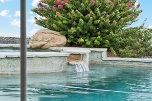 A pool with a waterfall feature, surrounded by a rock wall and a flowering bush. - Scottsdale Retreat Home w/ Pool and Patio (Scottsdale)