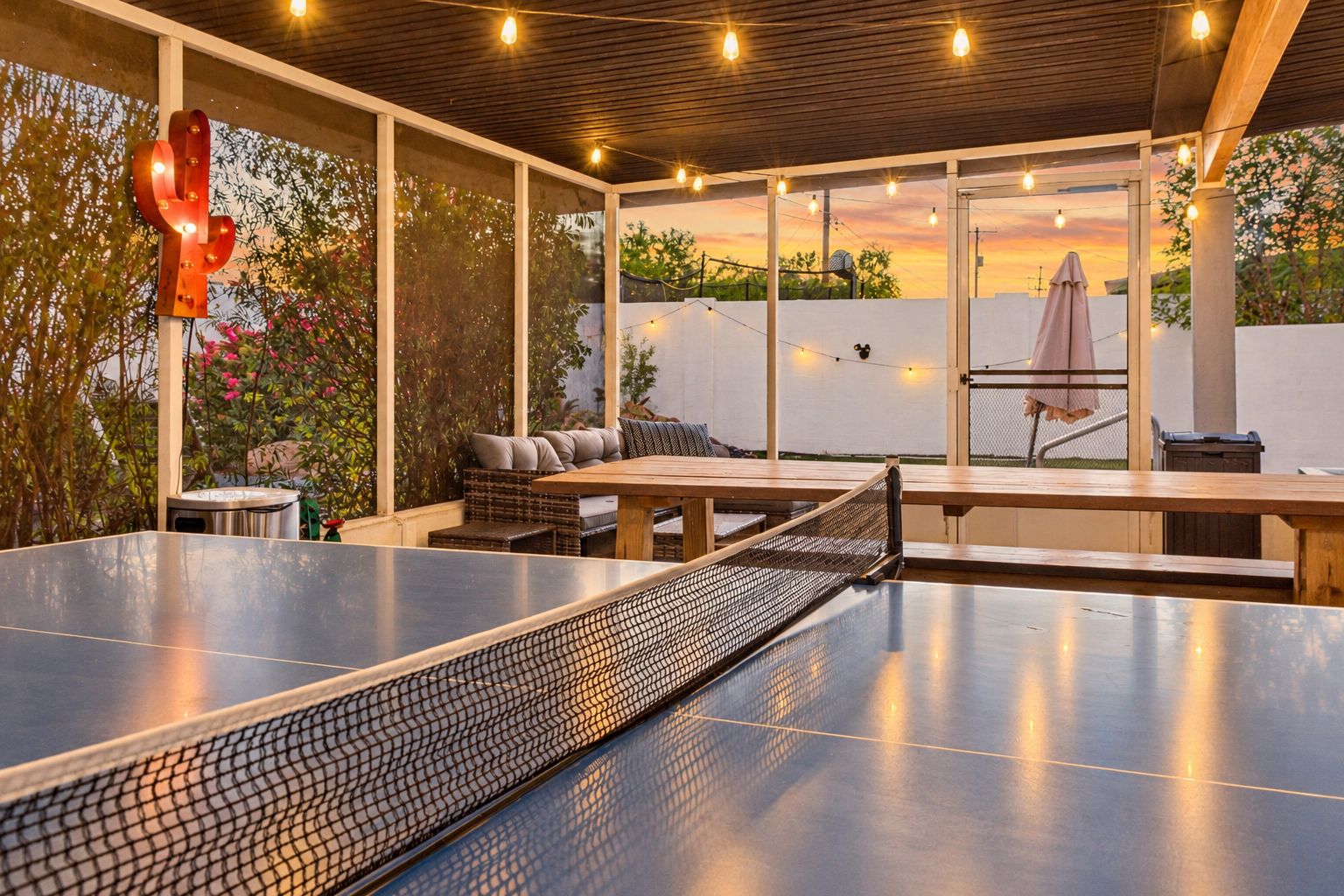 Un patio al aire libre con mesa de ping pong, asientos e iluminación con guirnaldas.