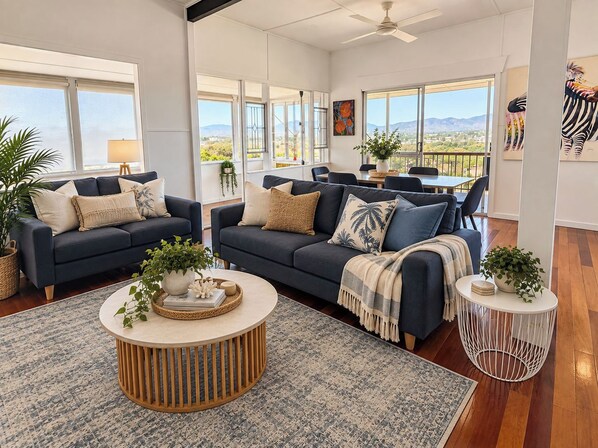 A spacious living room with a large window, a ceiling fan, and a dining area with a view. - Hillside Vista| West End Retreat w/Panoramic Views (West End)