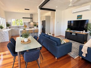 A modern living space with a dining area, a sofa set, a TV, and a kitchen. - Hillside Vista| West End Retreat w/Panoramic Views (West End)