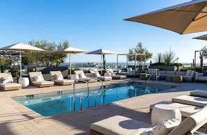 A poolside area with lounge chairs, umbrellas, and a view of the sea.