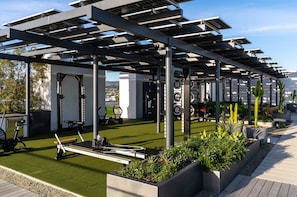 A rooftop gym with exercise equipment, solar panels, and planters.