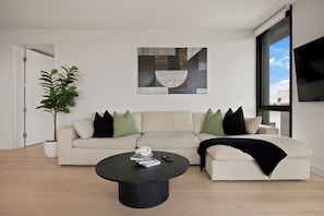 A modern living room with a beige sofa, a black coffee table, and a large abstract painting on the wall.