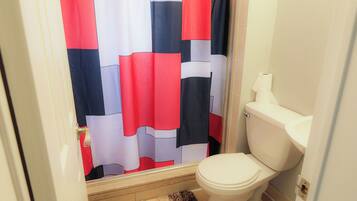 A bathroom with a toilet, a roll of toilet paper, and a shower curtain with a red, white, and blue pattern.