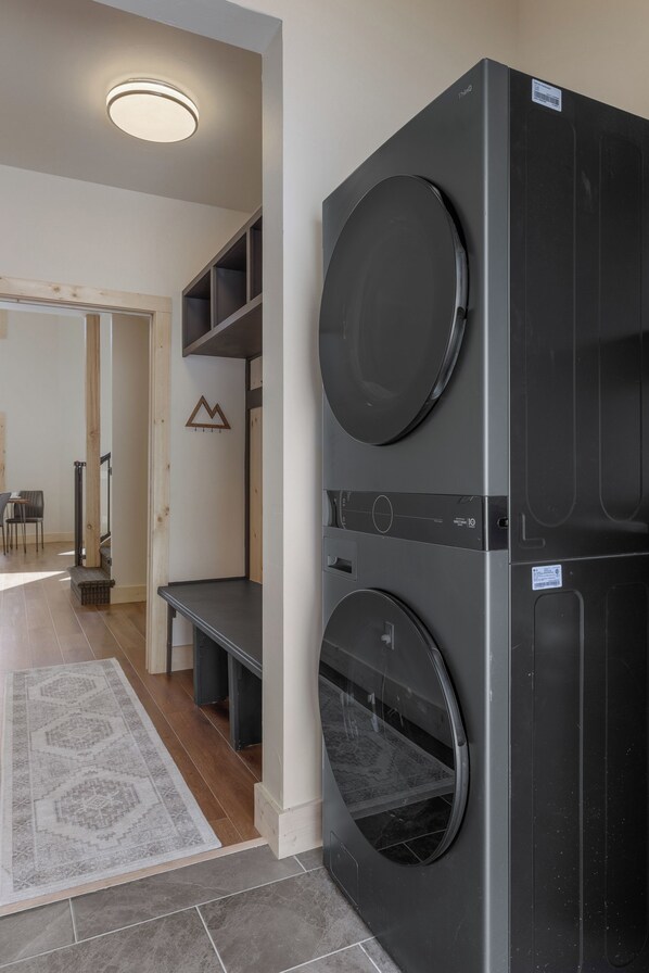 A laundry area with two stacked washing machines, a bench, and a small shelf unit. - Brand-New Mountain-Modern Build, Doggie Door to Dog Pen, Starlink, Fire Table (Fairplay)