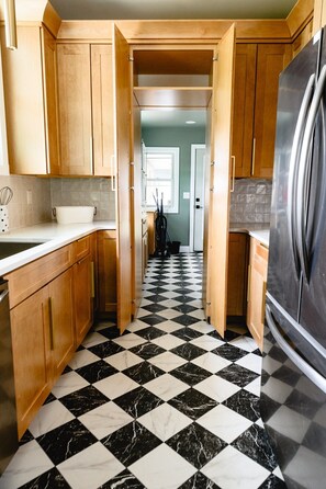 A kitchen with wooden cabinets, a black and white checkered floor, and a stainless steel refrigerator. - 3BR | Marathon | VA | Marshall (Huntington)