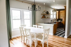 A dining area with a white table and chairs, a chandelier, and a kitchen with wooden cabinets and a checkered floor. - 3BR | Marathon | VA | Marshall (Huntington)