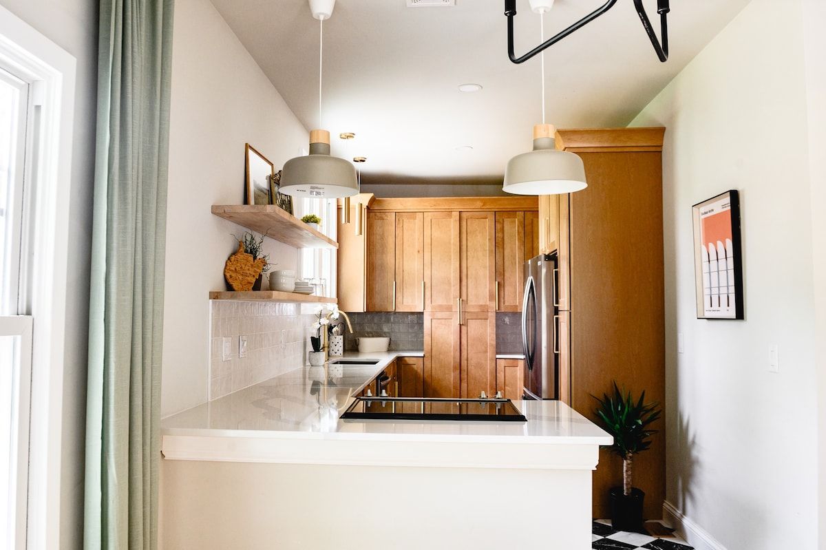 A modern kitchen with wooden cabinets, a stainless steel refrigerator, and pendant lighting.