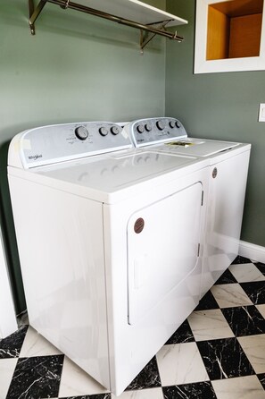 A white Whirlpool washer and dryer unit with control knobs, set against a green wall and a black and white tiled floor. - 3BR | Marathon | VA | Marshall (Huntington)