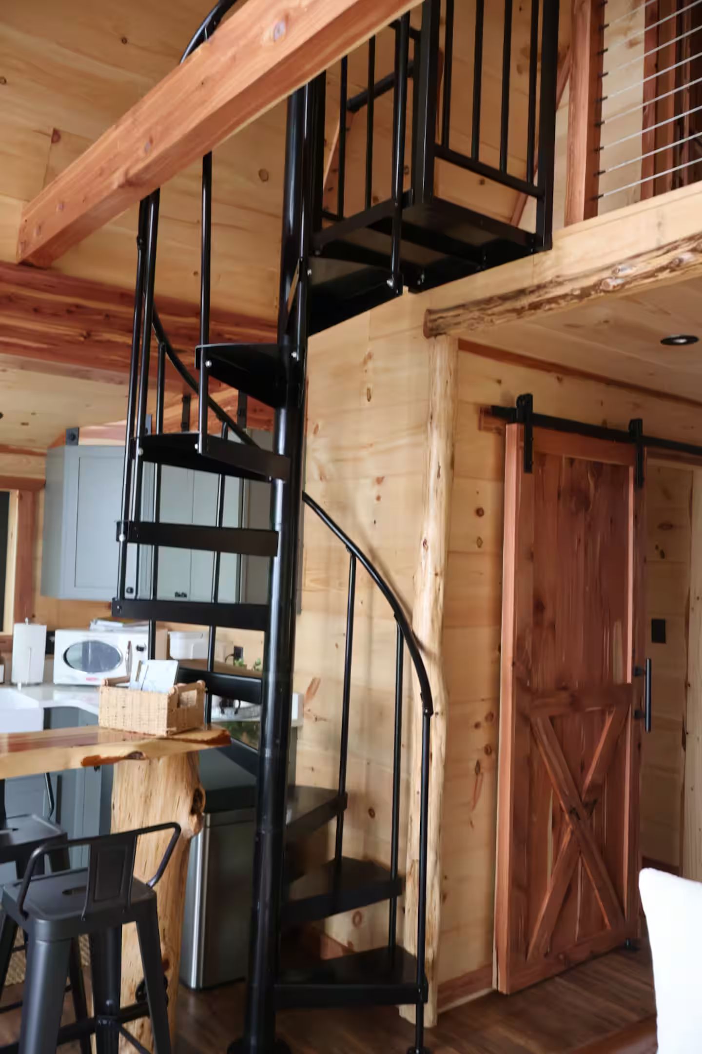 Un escalier en colimaçon, avec une structure intérieure en bois et une rampe en métal noir.