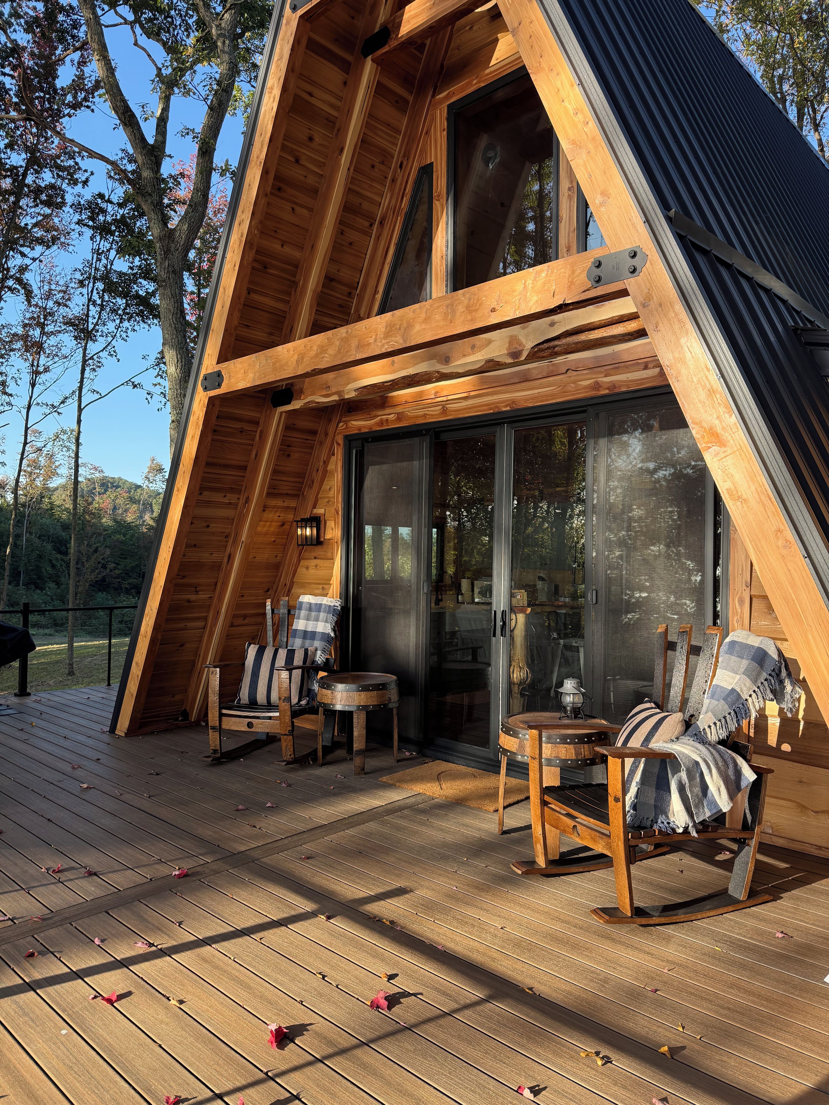 Una struttura a forma di A in legno con una veranda, due sedie, un tavolino e una porta vetrata che dà all'interno.