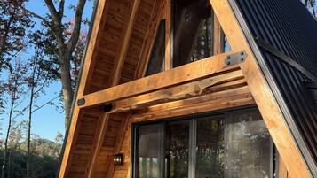 Una struttura a forma di A in legno con una veranda, due sedie, un tavolino e una porta vetrata che dà all'interno.