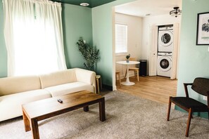 A living room with a sofa, a coffee table, a chair, a plant, and a laundry area with a washing machine. - 2BR in Barboursville, Near Mall, Parks, & Marshall (Huntington)