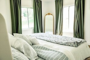 A bedroom with a bed, a large mirror, and green curtains.