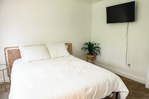 A bedroom with a bed, a television mounted on the wall, and a potted plant.