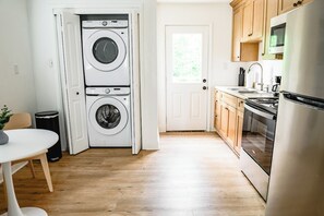A laundry room with stacked washers and dryers, a white door, and a kitchen area with wooden cabinets and appliances.