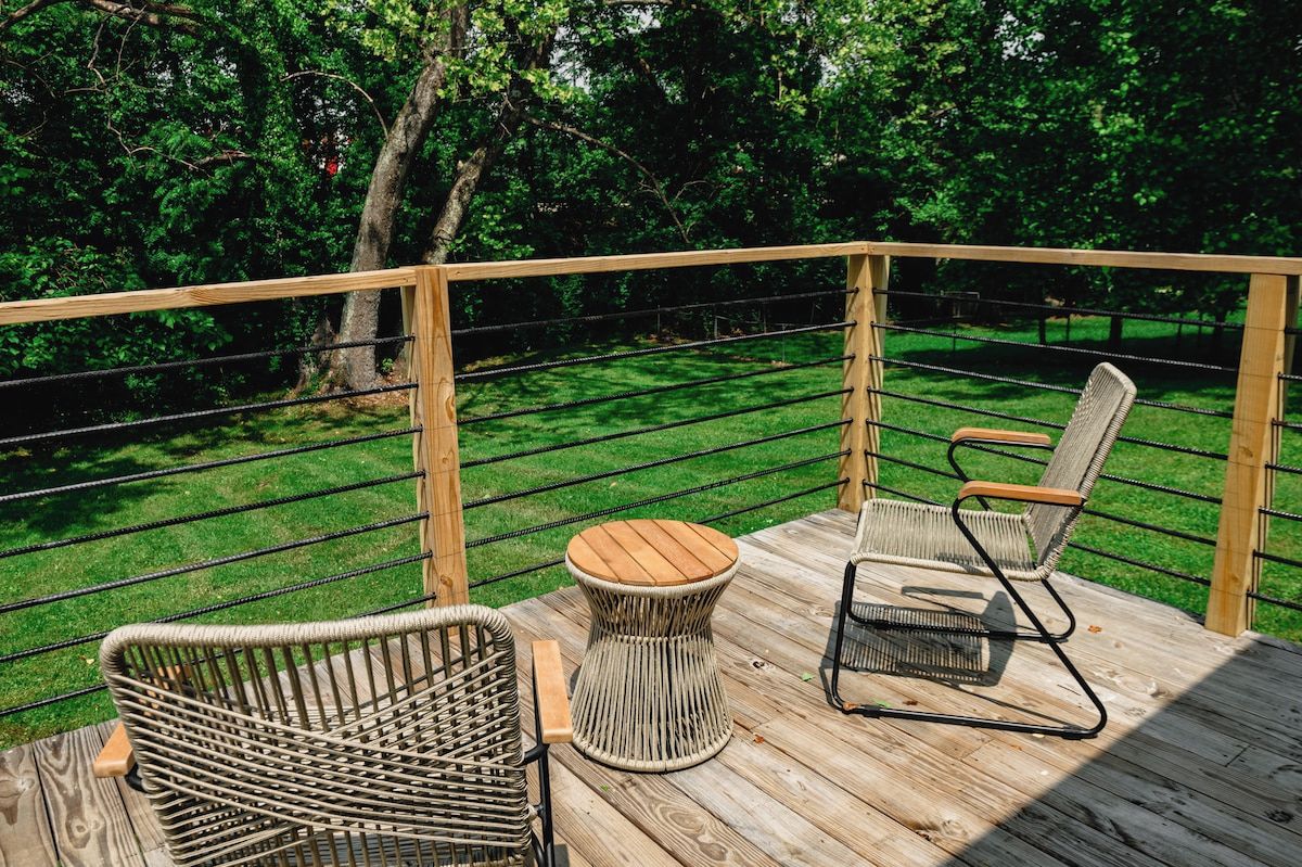 Une terrasse en bois, meublée de meubles en osier, avec vue sur une zone verdoyante.