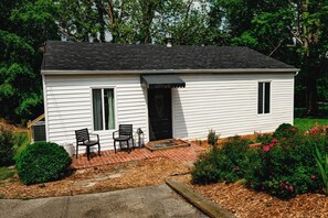 A single-story white house with a black roof, a front door, and two windows. There is a brick pathway leading to the entrance, and two chairs are placed outside. - 2BR in Barboursville, Near Mall, Parks, & Marshall (Huntington)