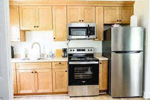 A kitchen with wooden cabinets, a stainless steel refrigerator, a microwave, a stove, and a sink.
