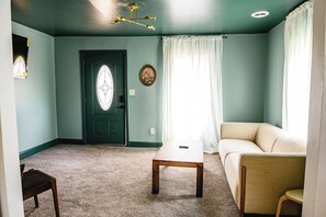 A room with a door, a table, a sofa, and a small chair.