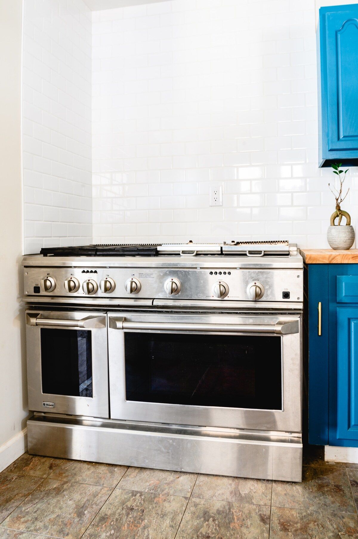 A stainless steel stove with four burners and two ovens, positioned in a kitchen with white subway tile backsplash and blue cabinets.