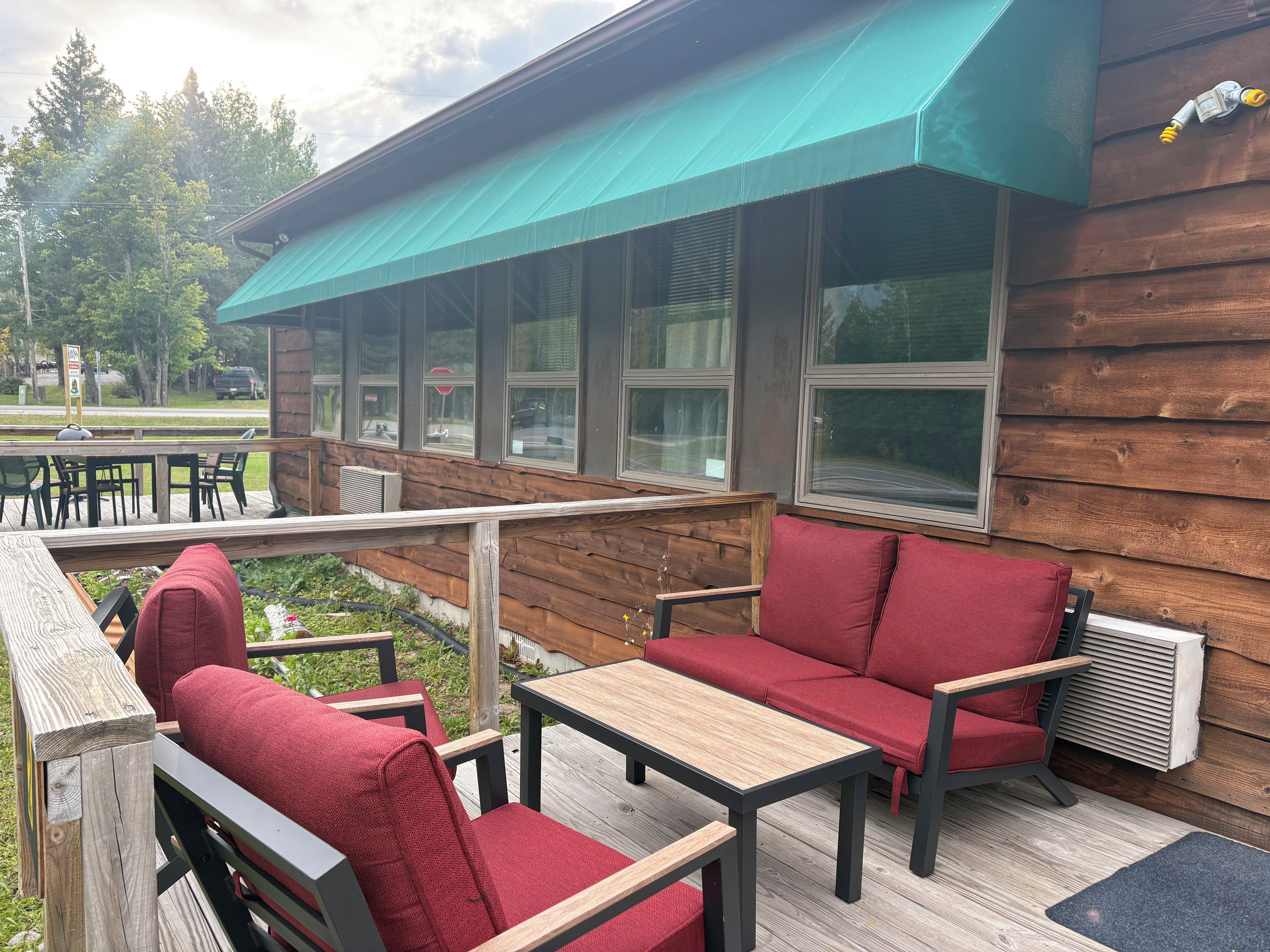 An outdoor seating area with red cushioned chairs and tables, a wooden deck, and a covered section with a green awning.