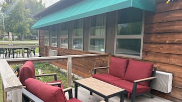 An outdoor seating area with red cushioned chairs and tables, a wooden deck, and a covered section with a green awning.
