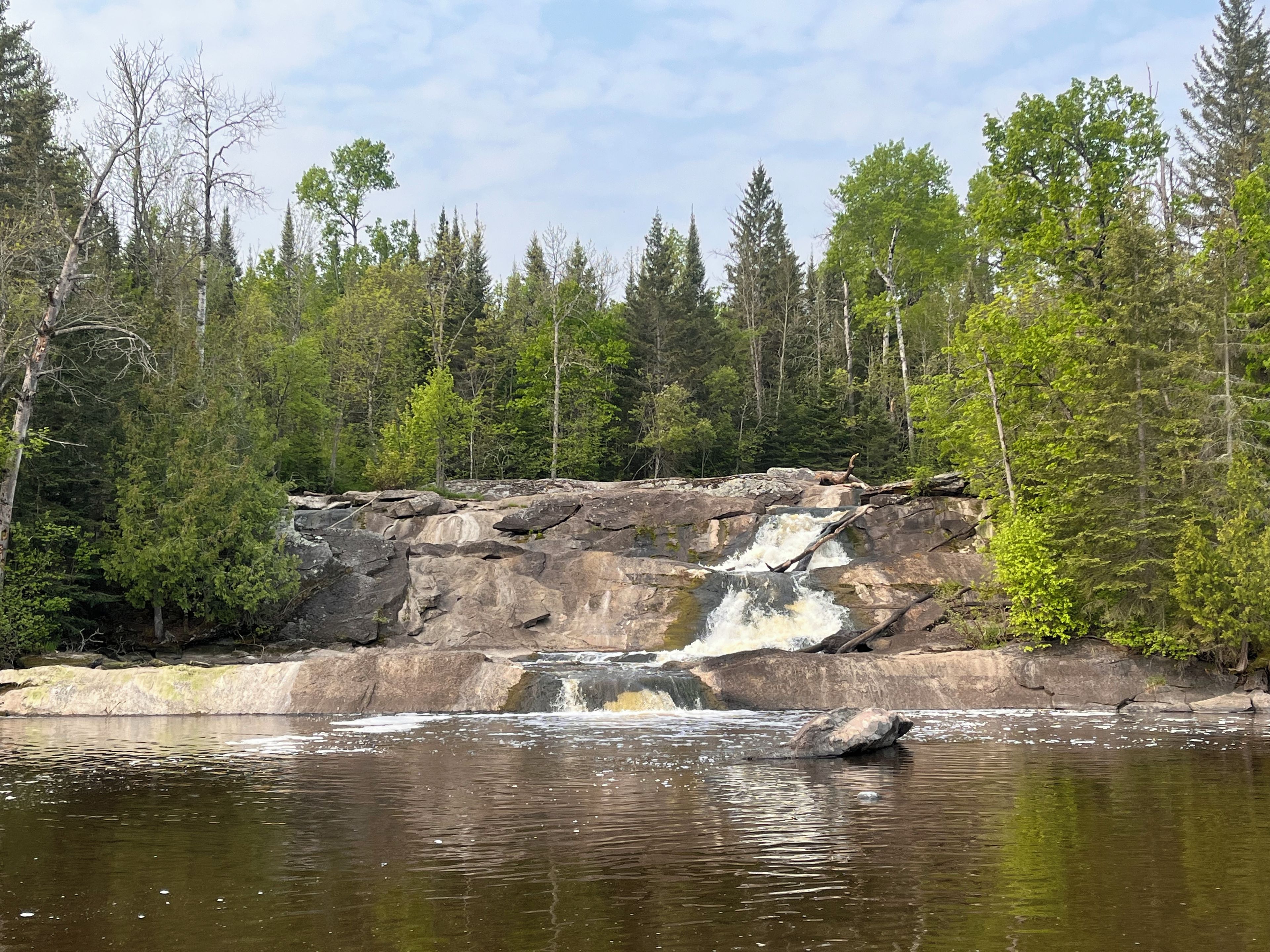 A natural landscape with a waterfall, rocky terrain, and dense forest.